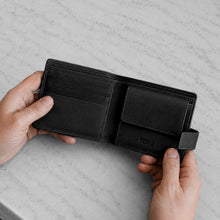 Load image into Gallery viewer, A black leather bifold wallet held open by two hands against a light gray marble surface. The wallet has multiple card slots on the left and a slip pocket on the right with an embossed logo that reads 'REDI'.