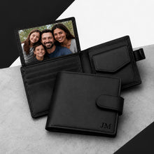 Load image into Gallery viewer, Black leather bifold wallet shown open and closed on a light gray surface with a black-and-white geometric background. The wallet has card slots, a photo ID window holding a family portrait, a flap pocket, and a strap closure.