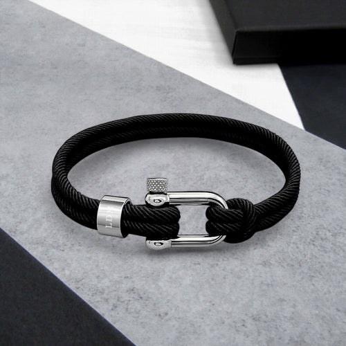 Black braided cord bracelet with silver clasp on a gray surface
