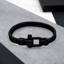 Load image into Gallery viewer, Black braided bracelet with a clasp on a gray surface