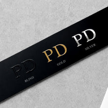 Load image into Gallery viewer, Black leather sample strip featuring debossed PD logo with blind, gold and silver foil finish variations.