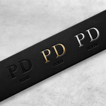 Load image into Gallery viewer, A close-up of a black rectangular product box or packaging strip on a light gray marble-like surface, featuring embossed 'PD' branding in black, gold, and silver with the words 'BLIND', 'GOLD', and 'SILVER' beneath.