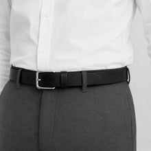 Load image into Gallery viewer, A close-up of a black leather belt with a silver buckle, worn around the waist of a person wearing a white button-down shirt and dark gray trousers.