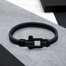 Load image into Gallery viewer, Black braided bracelet with a clasp on a gray surface