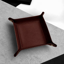 Load image into Gallery viewer, A Handmade Brown Leather Desk Tidy Valet Tray with raised corners and brass-tone snap fasteners, photographed on a light grey textured stone surface with a black and white geometric background